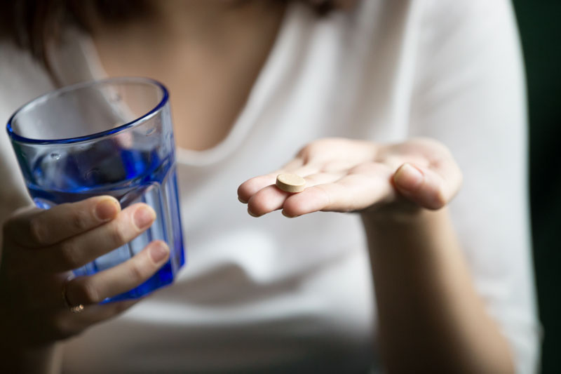 Mujer tomando una pastilla con un vaso de agua.